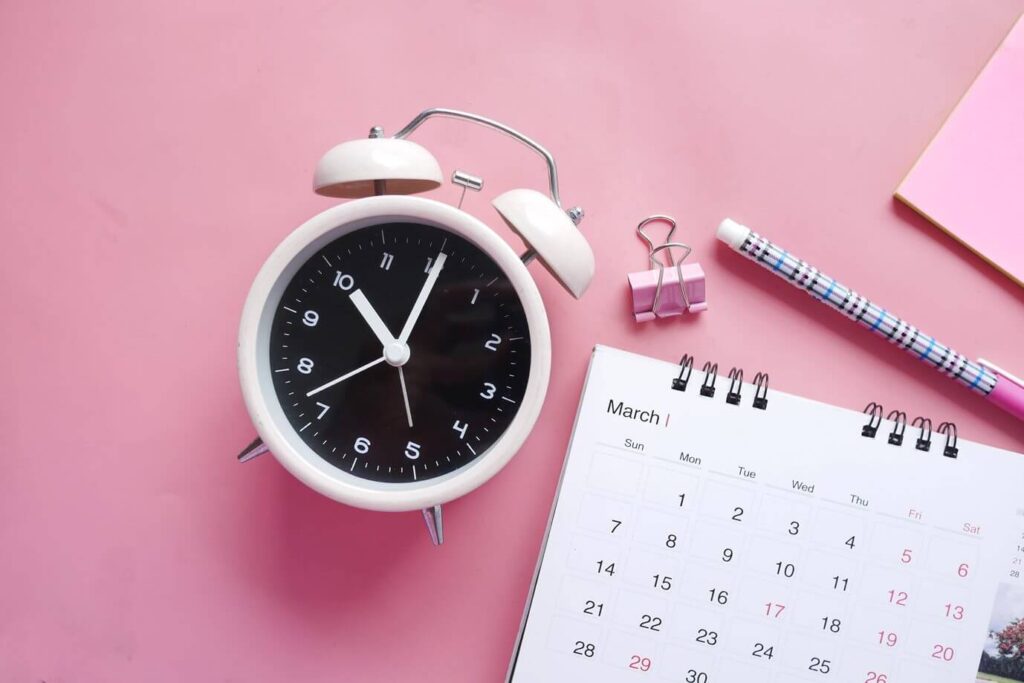 foto de um relógio, calendário e lápis em cima do que parece ser uma mesa
