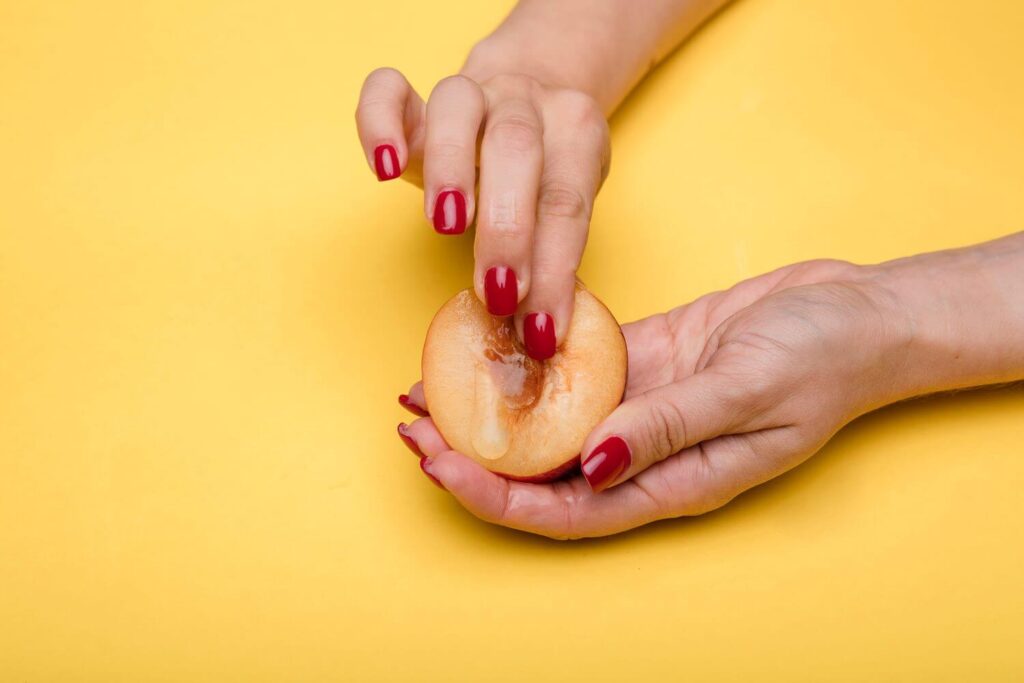 mãos, que parecem femininas, segurando um pêssego. O pêssego representa uma vagina e mão está apertando a fruta