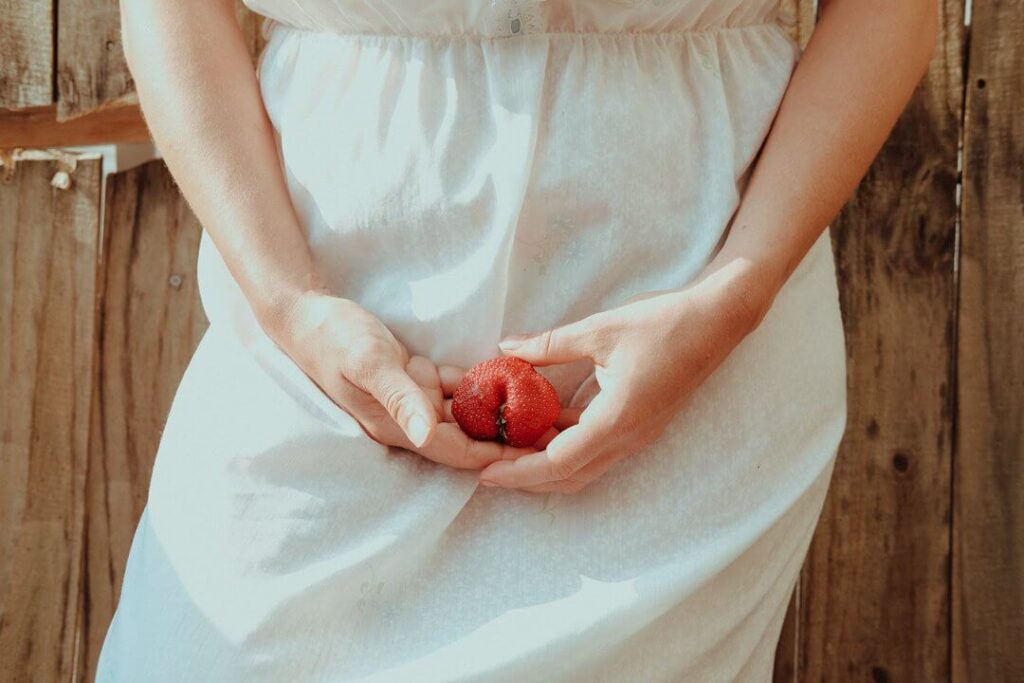 mulher segurando um morango, com formato de coração, a frente do seu útero 