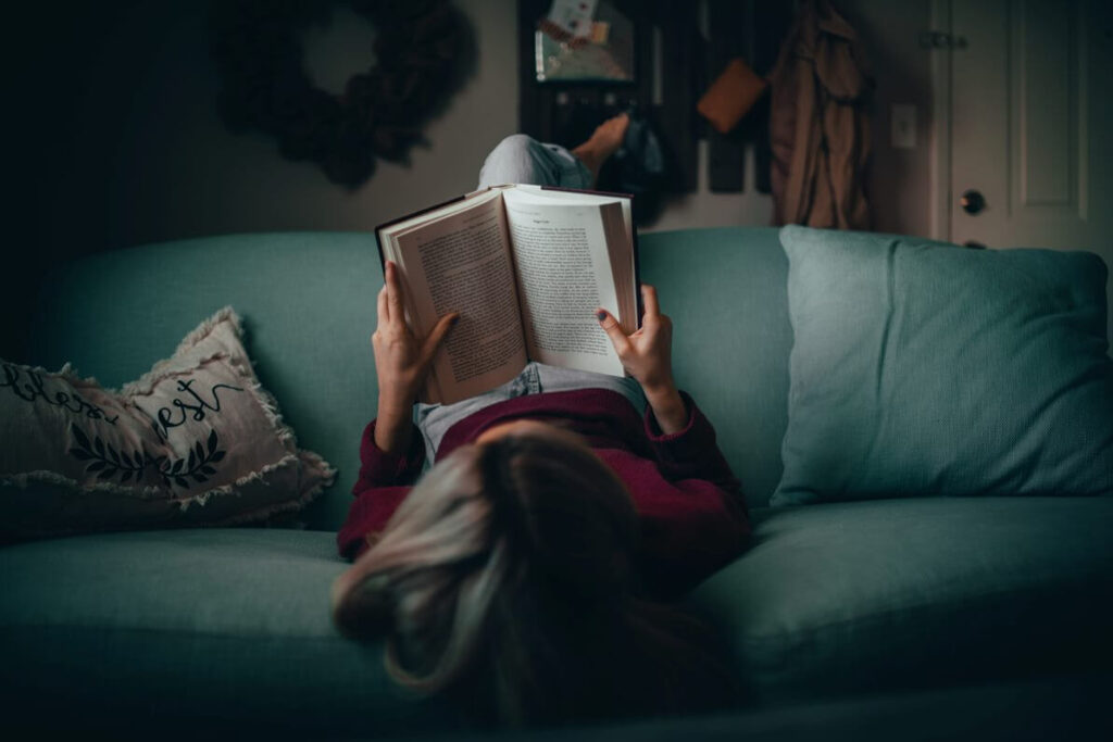 mulher deitada de cabeça para baixo em um sofá lendo um livro