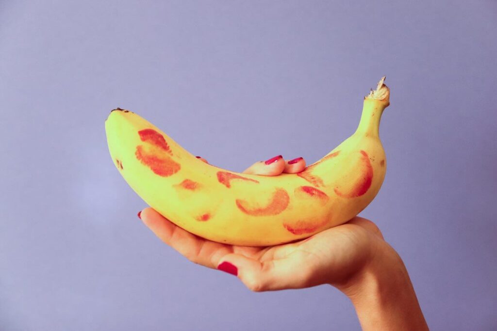 uma mão segurando uma banana com a casca cheia de marcas de batom 