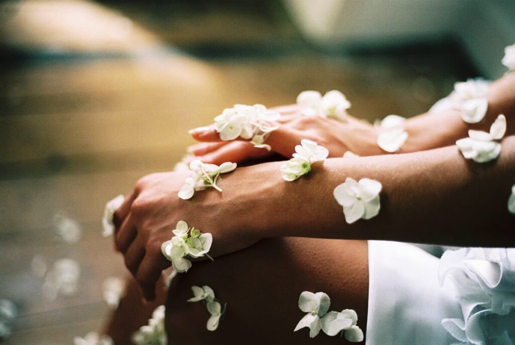 A foto foca nos braços e pernas de uma mulher. Há flores espalhadas pelas mãos, braços e pernas da mulher.