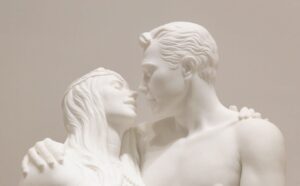 Escultura de mármore branco de um homem e uma mulher. Eles estão de abraçando de olhos fechados. Suas cabeças estão alinhadas e eles estão a ponto de se beijarem.