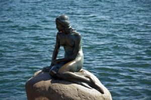 escultura de uma sereia sentada em uma pedra. A foto da escultura foi tirada de uma forma que a pedra parece estar no meio do mar