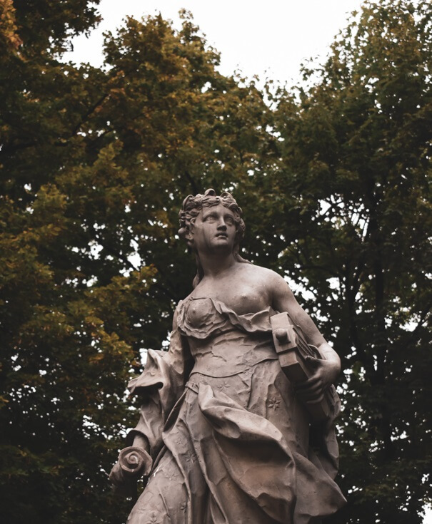 estatua da Caliope ao ar livre. Ela segura um pergaminho e um instrumento musical em cada uma das mãos