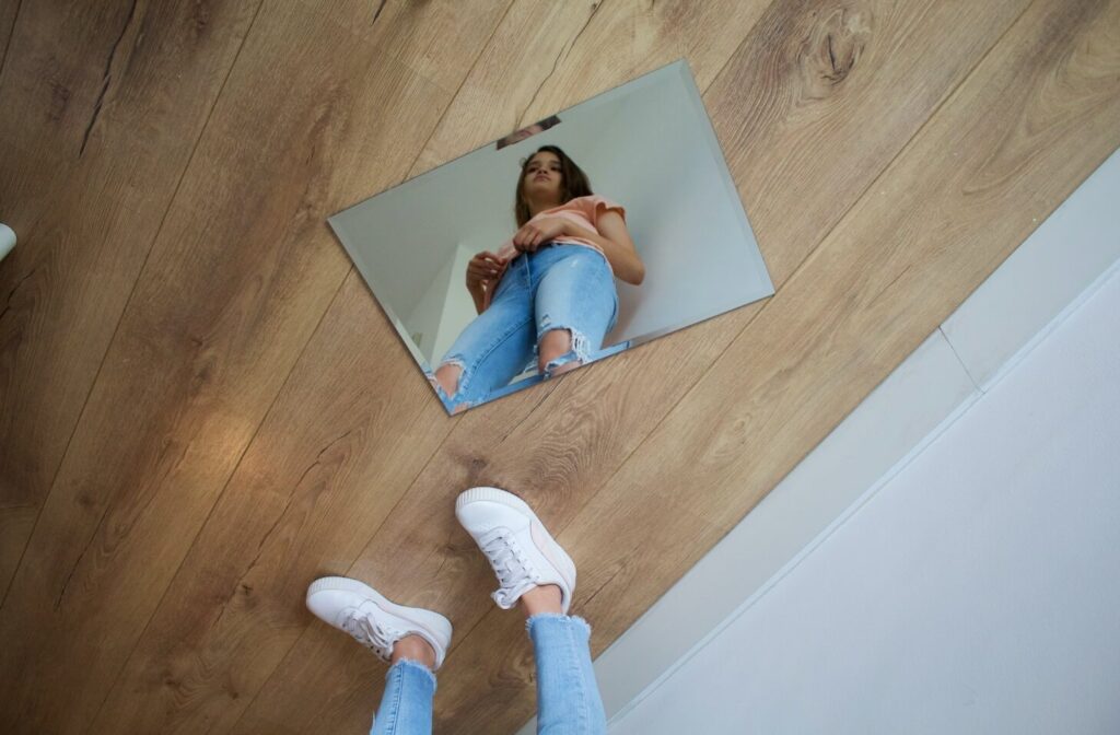 espelho pequeno no chão está refletindo uma mulher que está em pé ao lado do espelho.